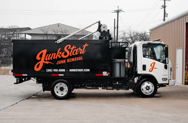 A white JunkStart junk removal truck with a black bed and orange branding is parked on concrete.