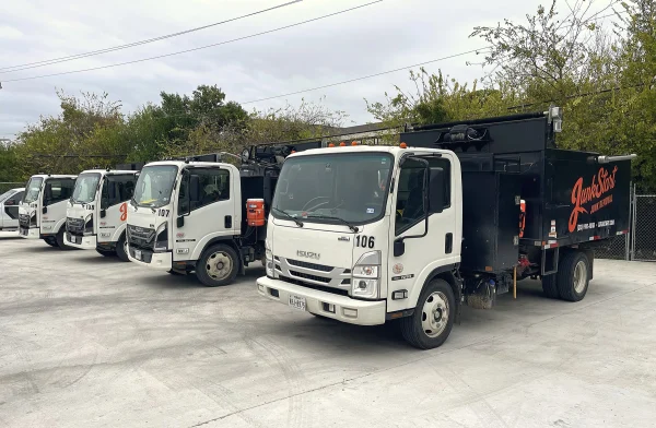 Several white Isuzu JunkStart junk removal trucks are parked neatly in a row on a