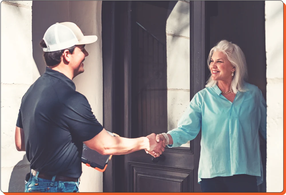 A service professional shakes hands with a smiling woman at her doorstep.