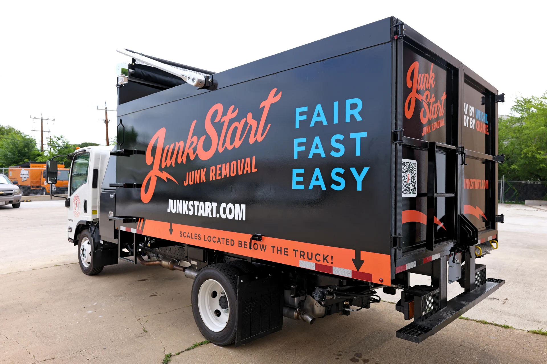 Black JunkStart junk removal truck with orange and blue branding, parked outdoors. TITLE:
