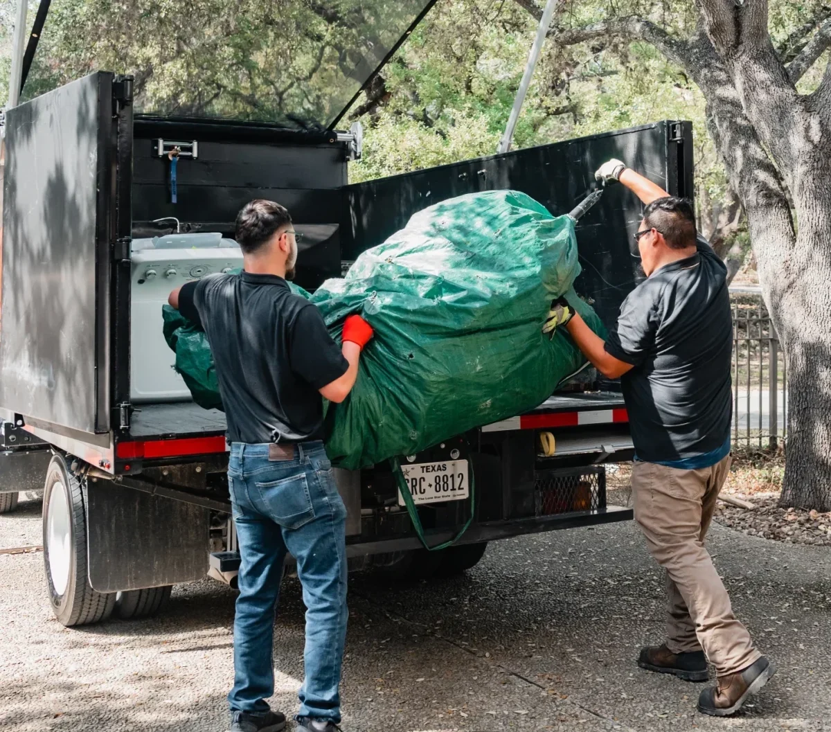 Professional junk removers load a washing machine and large green bag into a truck. TITLE: