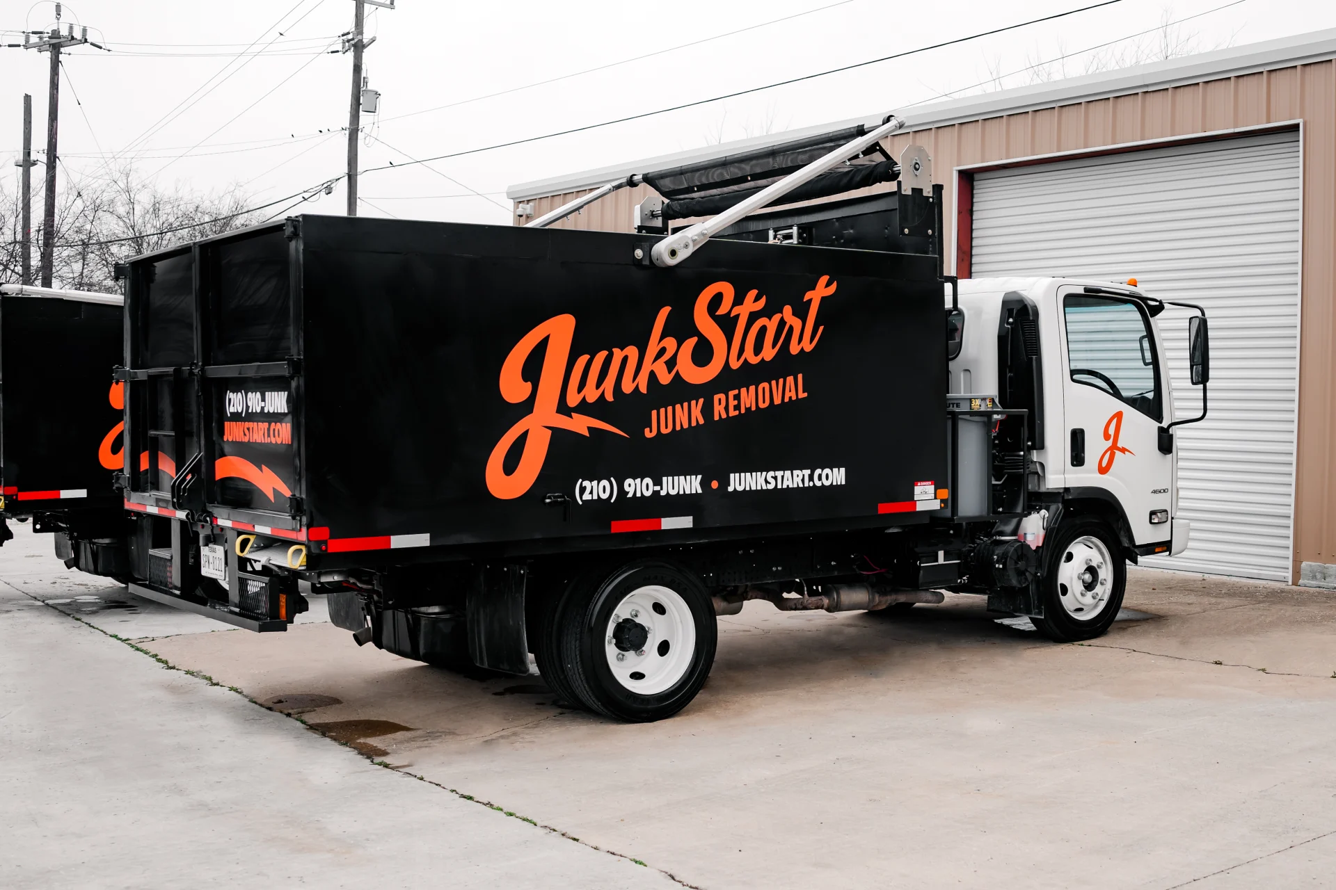 A black JunkStart junk removal truck with orange branding is parked outside a commercial building.